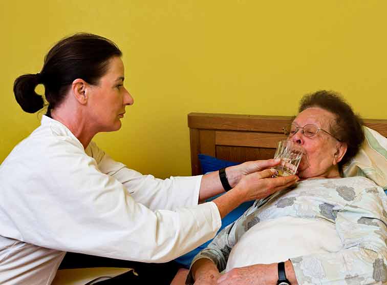 Pflegerin gibt Patientin Wasser zu trinken
